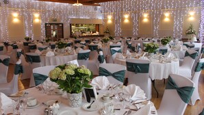 A banquet hall with round tables set for a formal event, each with white tablecloths, green sashes, and floral centerpieces. - Mackays Hotel Wick (Wick)