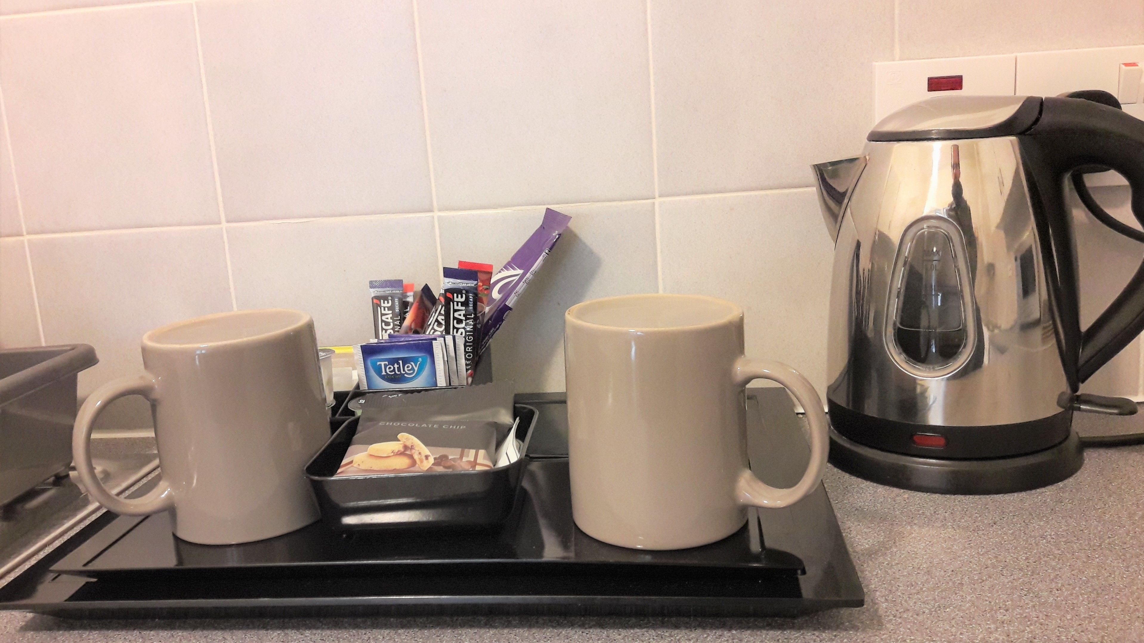Una encimera de cocina con dos tazas de café, una bandeja con sobres de café y una tetera.