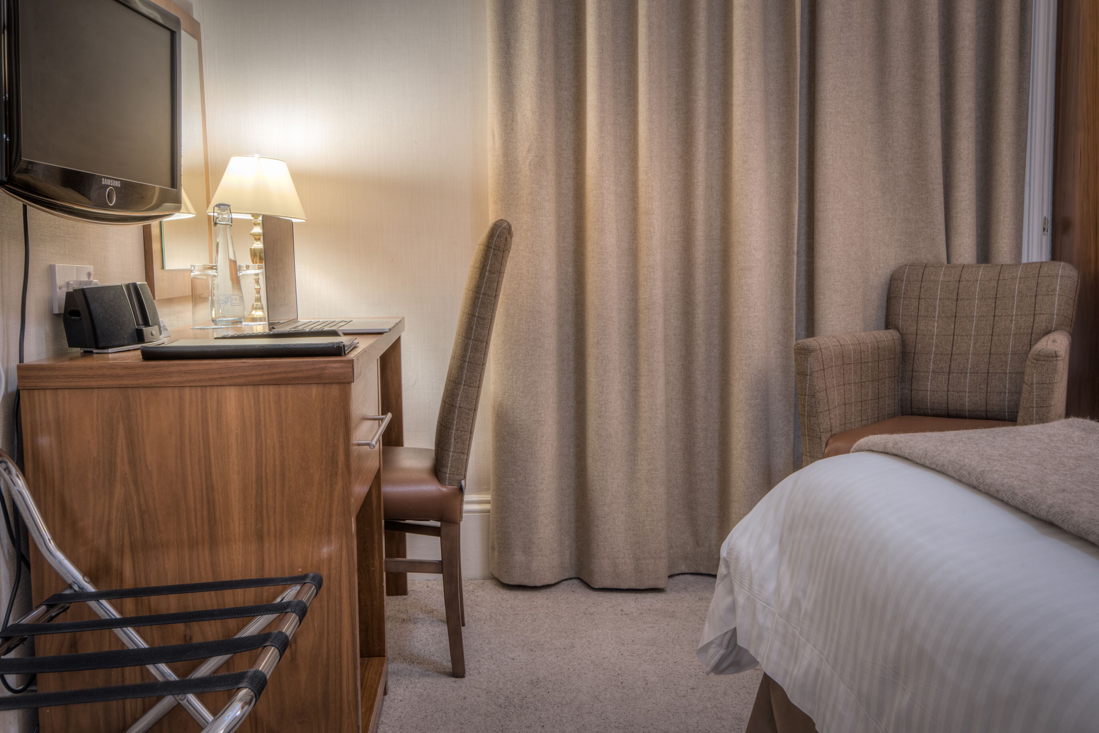 A hotel room with a desk, chair, bed, and curtains.