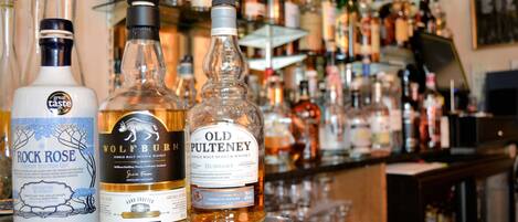 Trois bouteilles de whisky sont posées sur le comptoir d’un bar, avec un arrière-plan flou composé de diverses autres bouteilles.