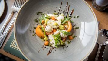 Un plato de comida con mozzarella, tomates y verduras, acompañado de cubiertos y una servilleta sobre una mesa.