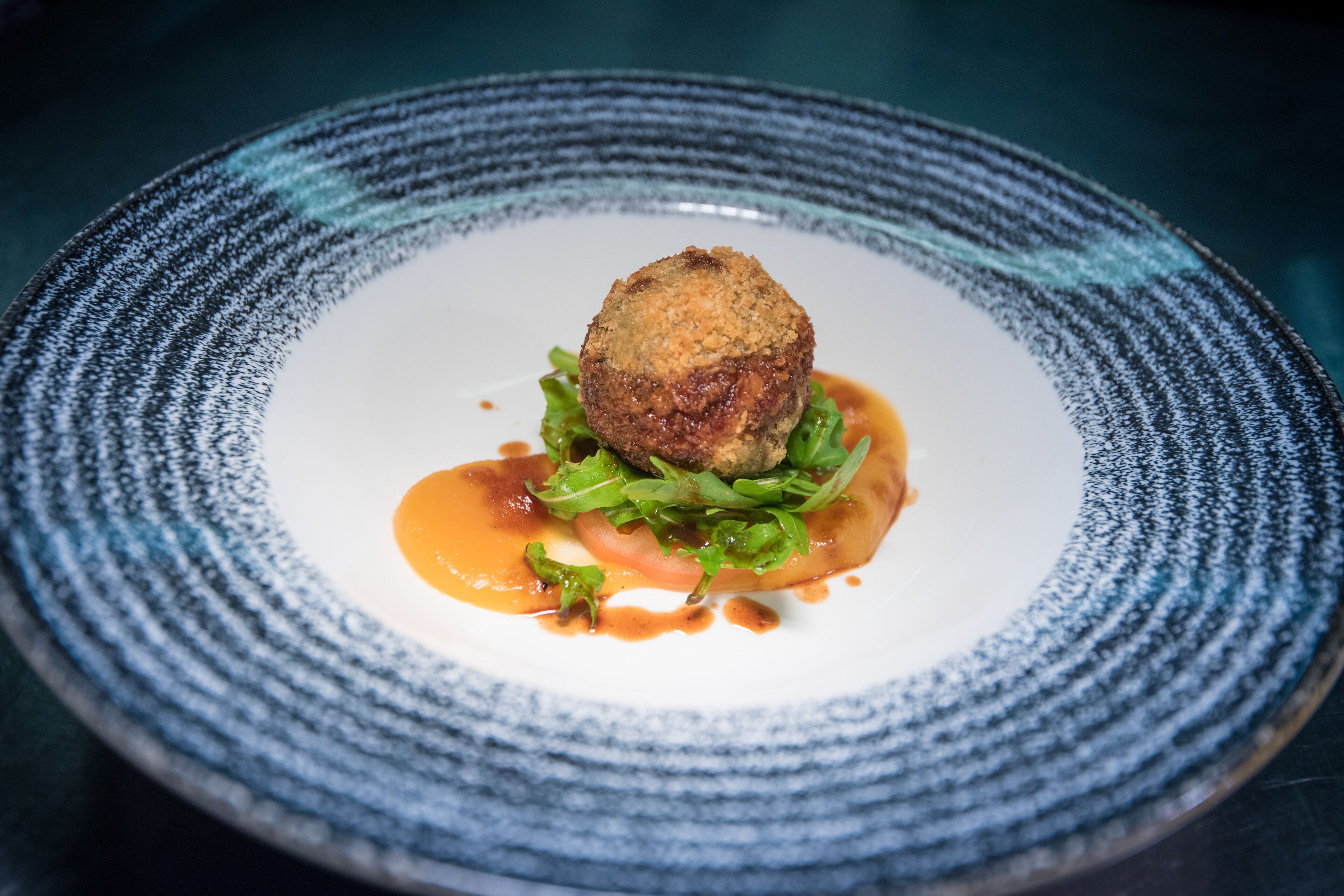 A plate with a food item, greens, and sauce.