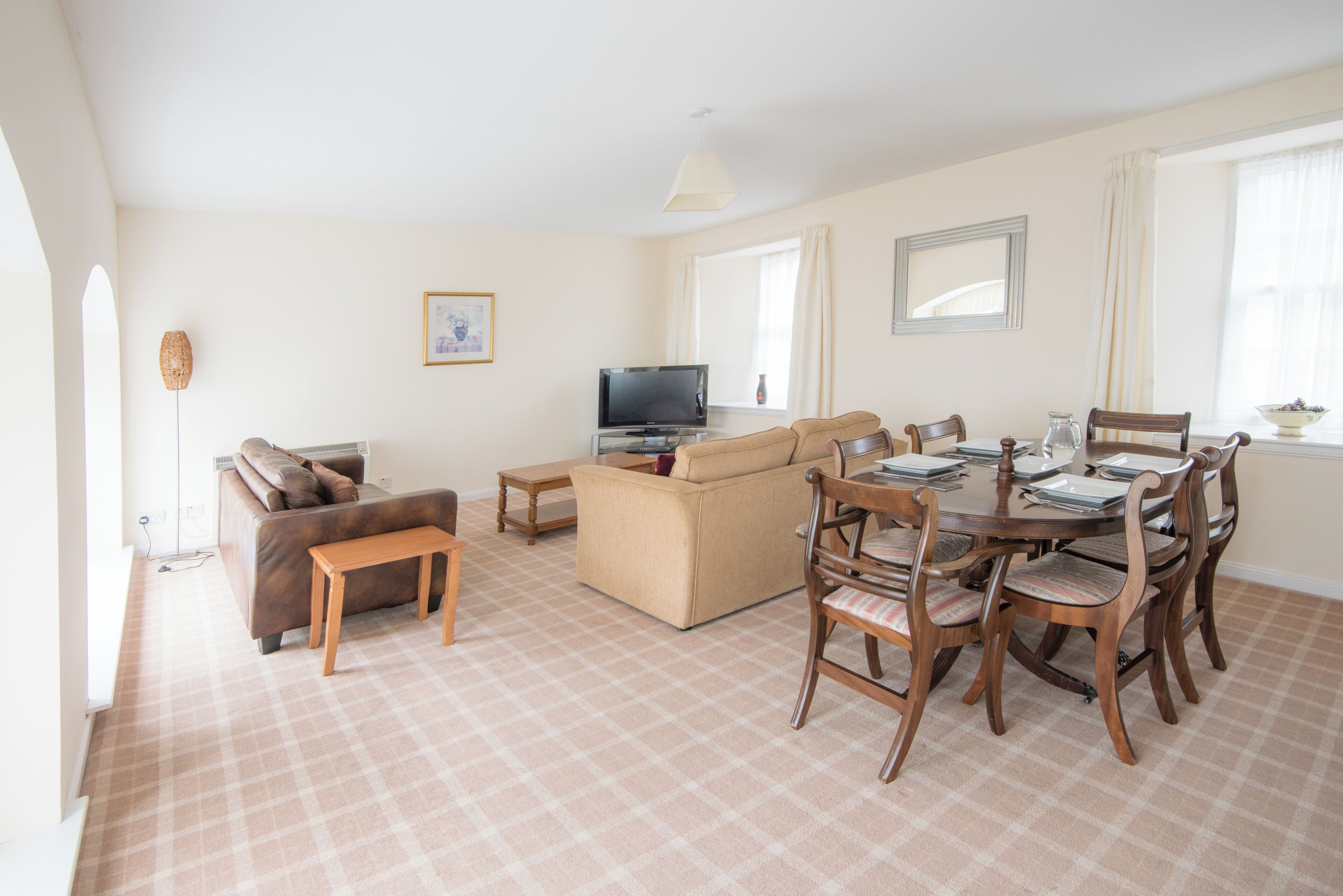 A living room with a sofa, a TV, a dining table with chairs, and a carpeted floor.