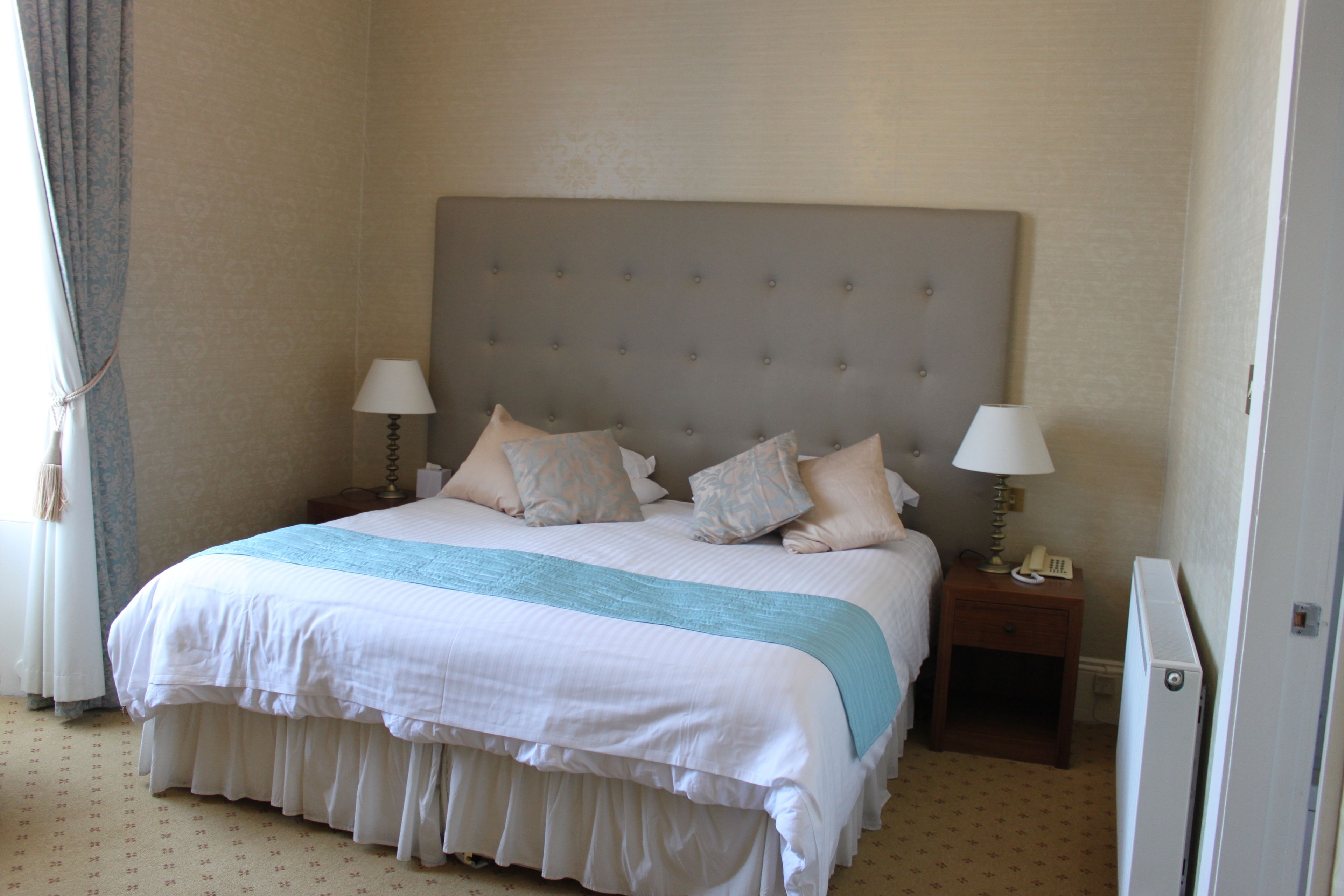 A neatly made bed with a grey headboard, two bedside tables with lamps, and a patterned carpet.