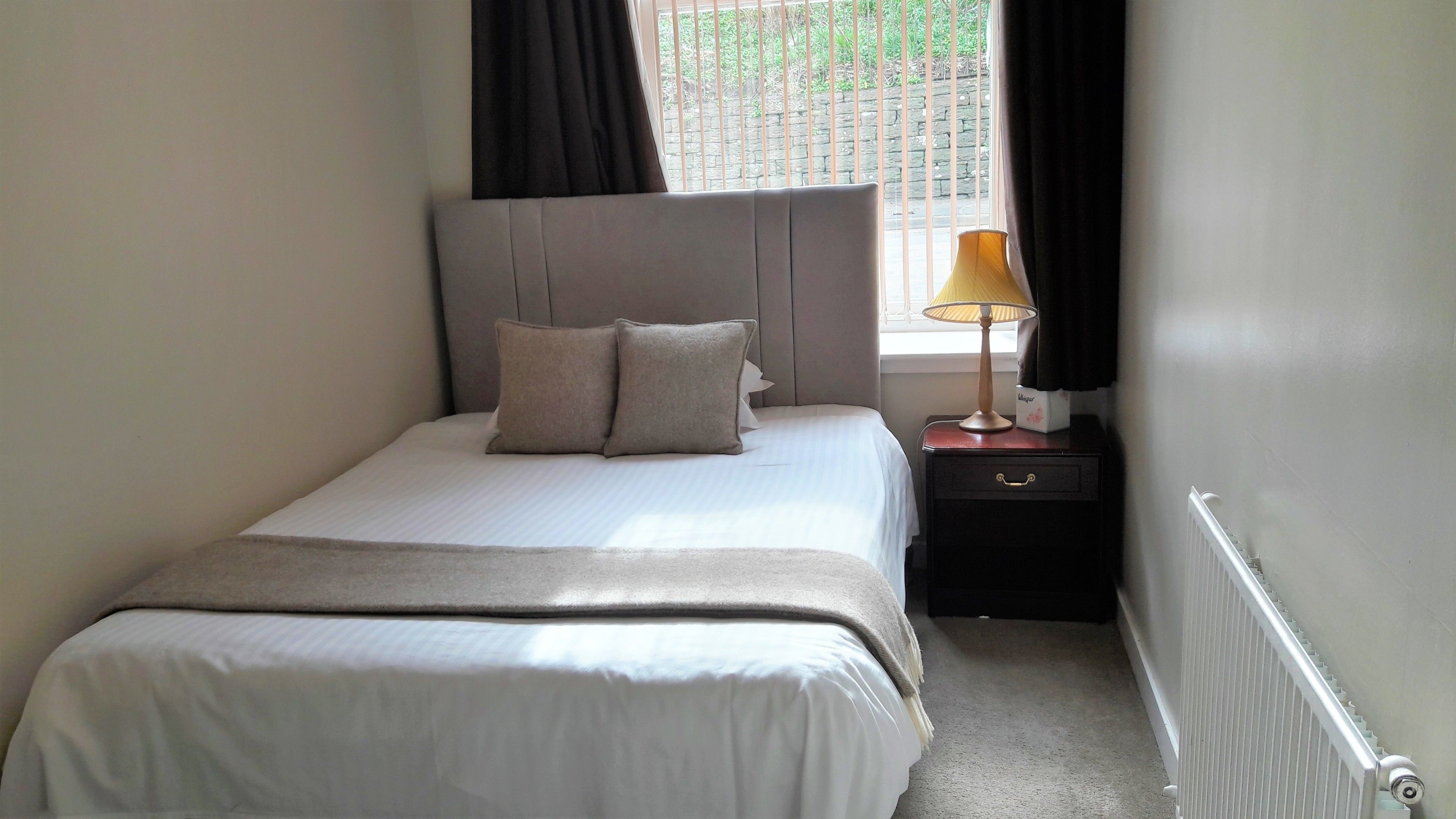 A neatly made bed with a headboard, two pillows, and a bedside table with a lamp.