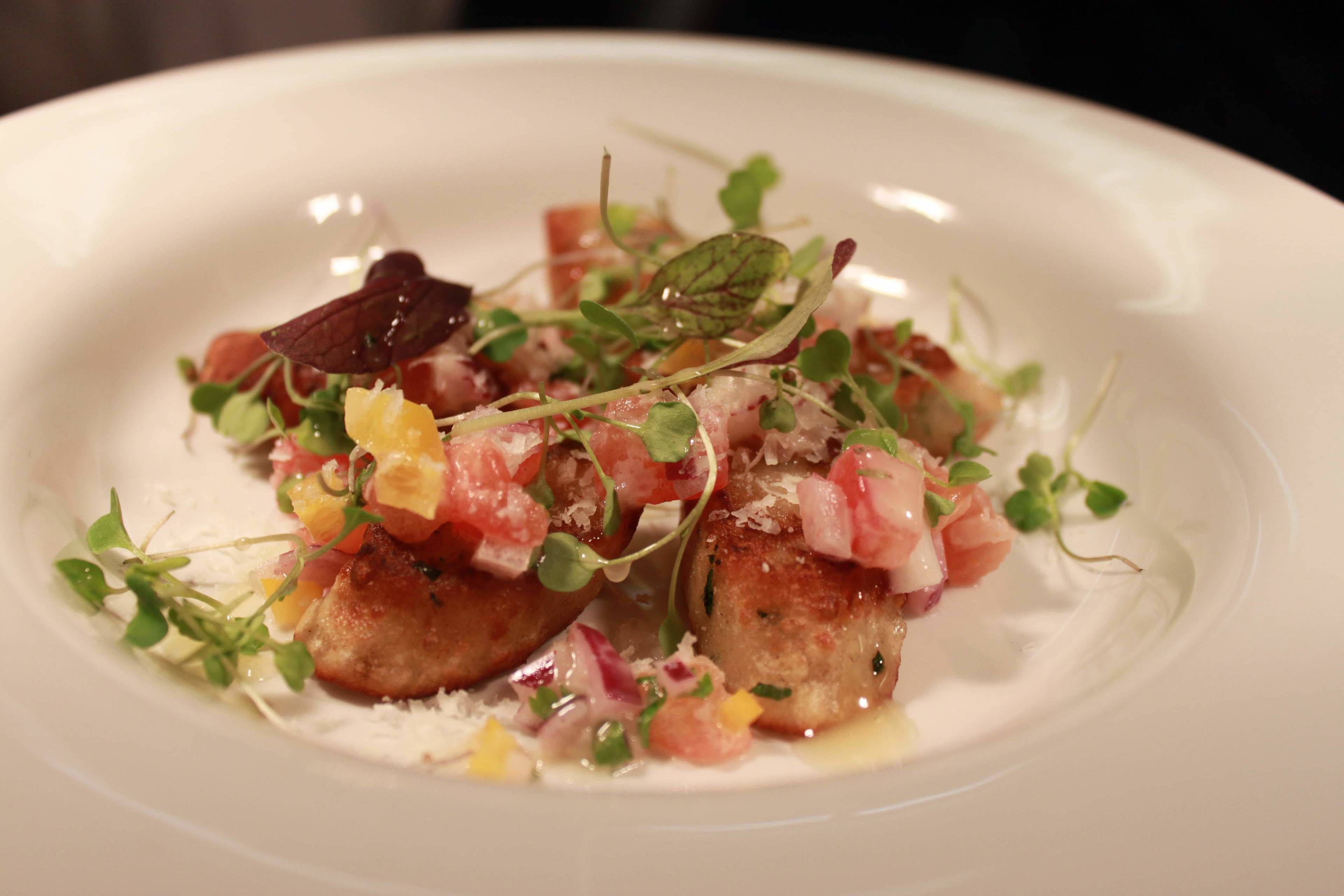 A white plate with a dish of seared scallops, diced tomatoes, and microgreens.