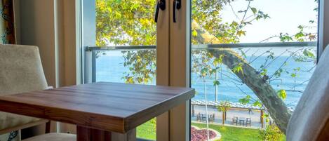 A room with a wooden table and a view of the sea through large windows.