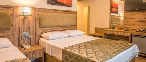A hotel room with two beds, wooden headboards, a desk with a mirror, and artwork on the walls.