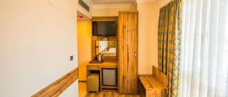 Una habitación de hotel compacta con kitchenette, un pequeño rincón de descanso y una ventana con cortinas estampadas.