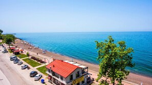 A coastal hotel with a red-roofed building, a parking lot, and a beach view.