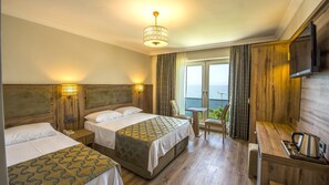A hotel room with two beds, a desk, a chair, a television, and a view of the sea.