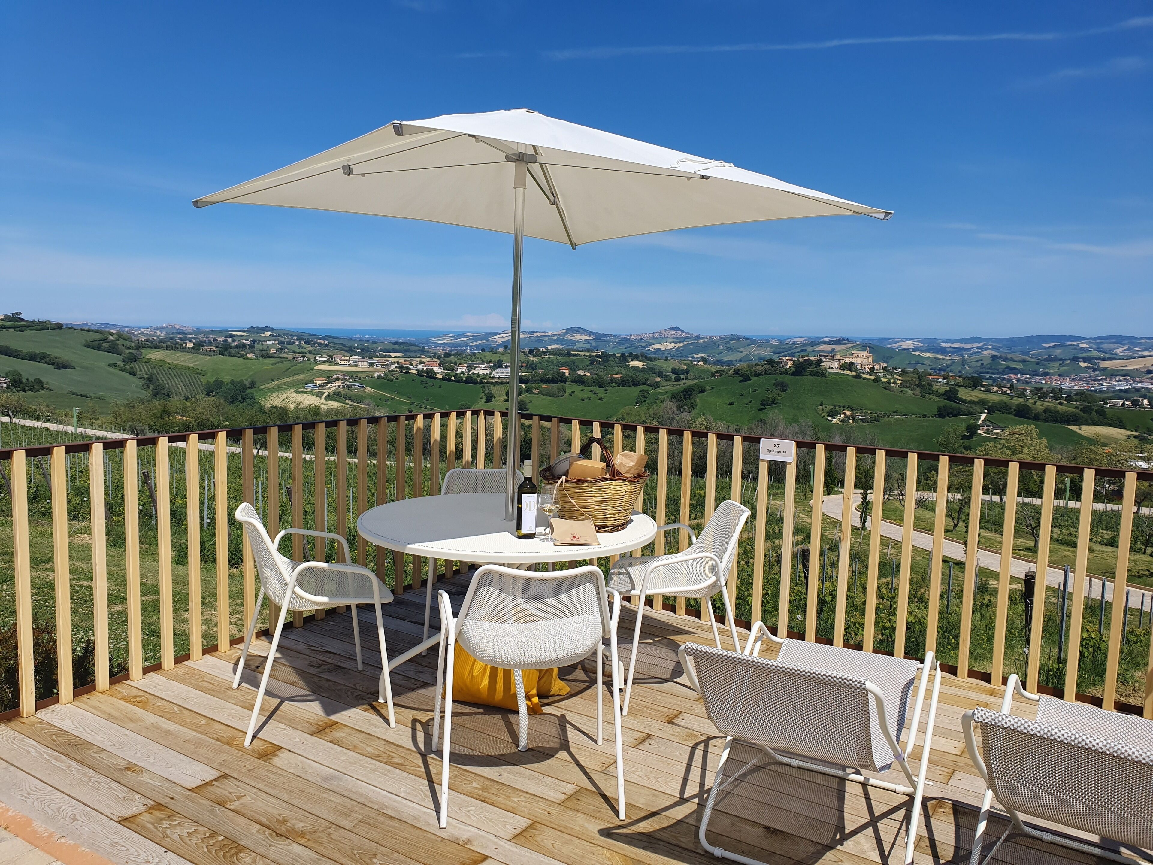 A wooden deck with a round table and chairs, an umbrella, and a bottle of wine.