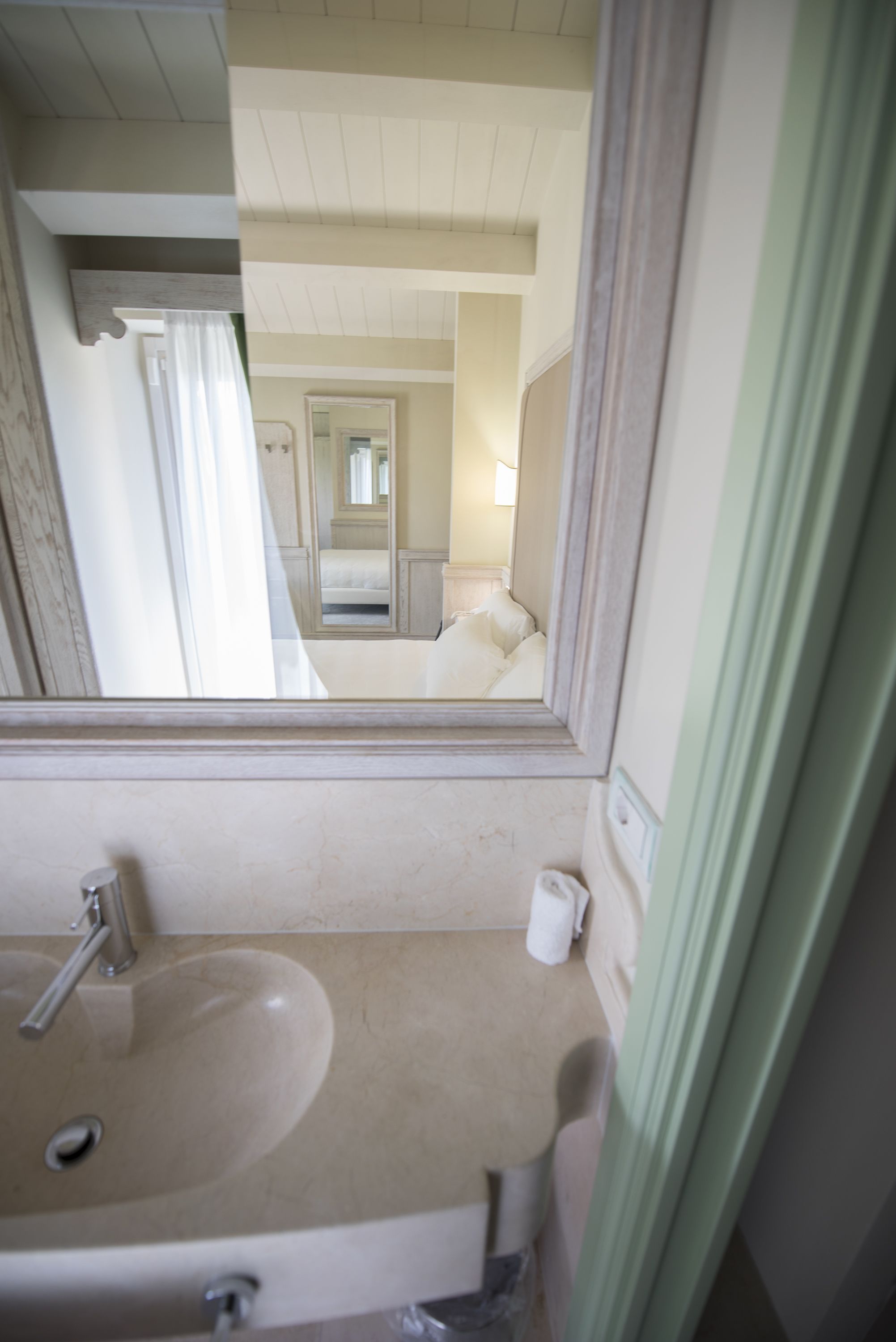 A bathroom with a sink, mirror, and a view into a bedroom with a bed and a nightstand.