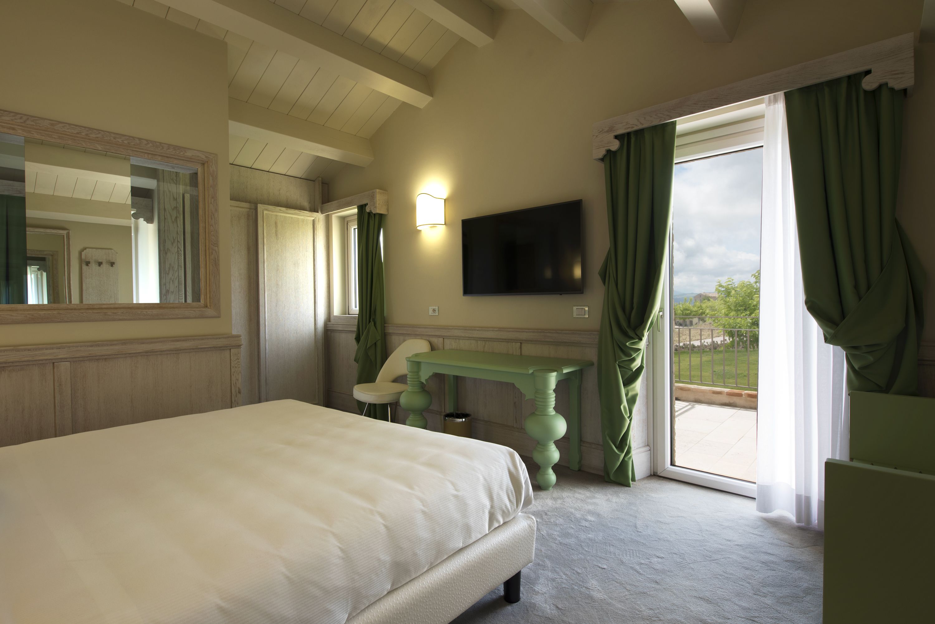 Un dormitorio con cama, tocador verde, televisor y vista al exterior.