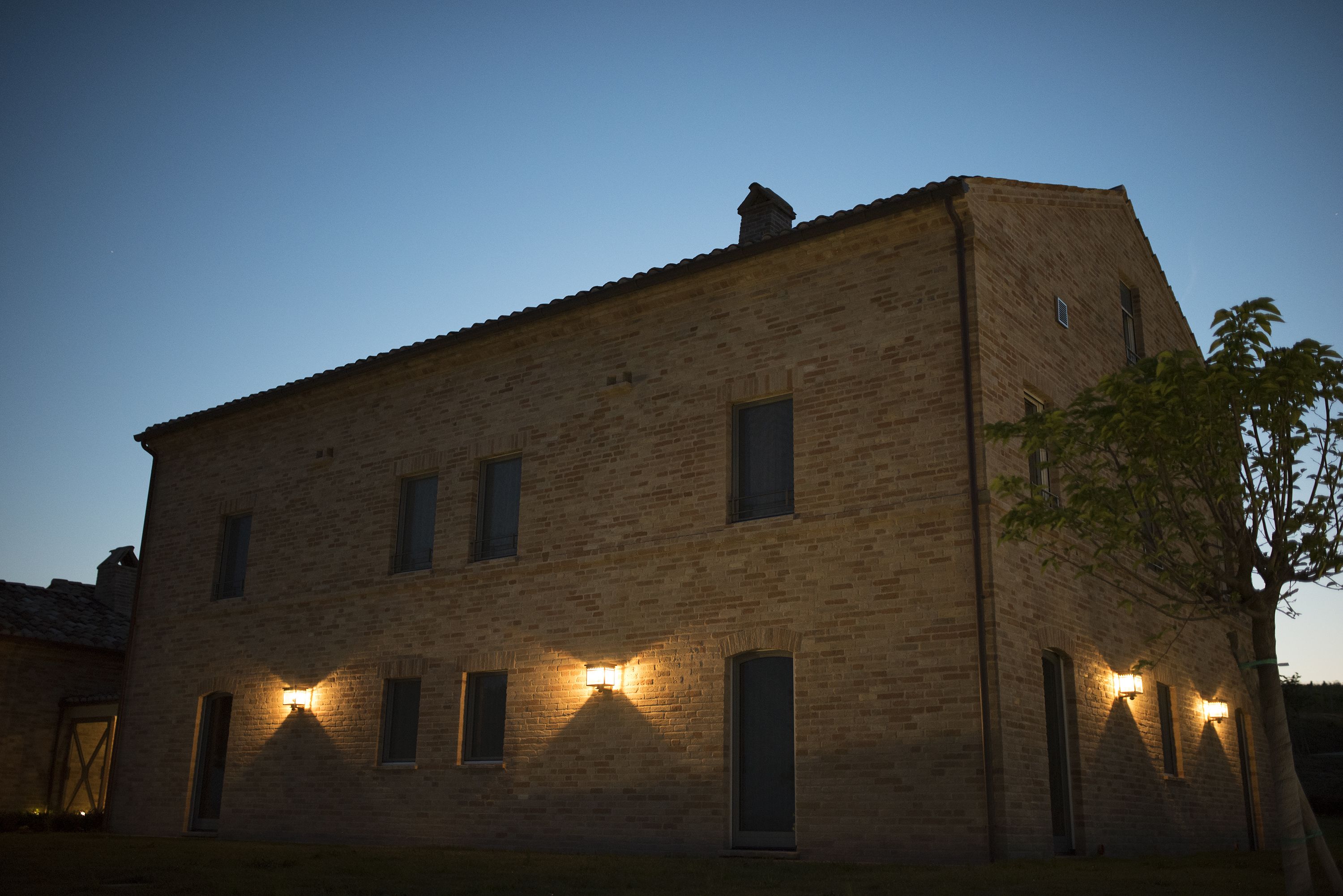 A brick building with multiple windows and a door, illuminated by exterior lights.