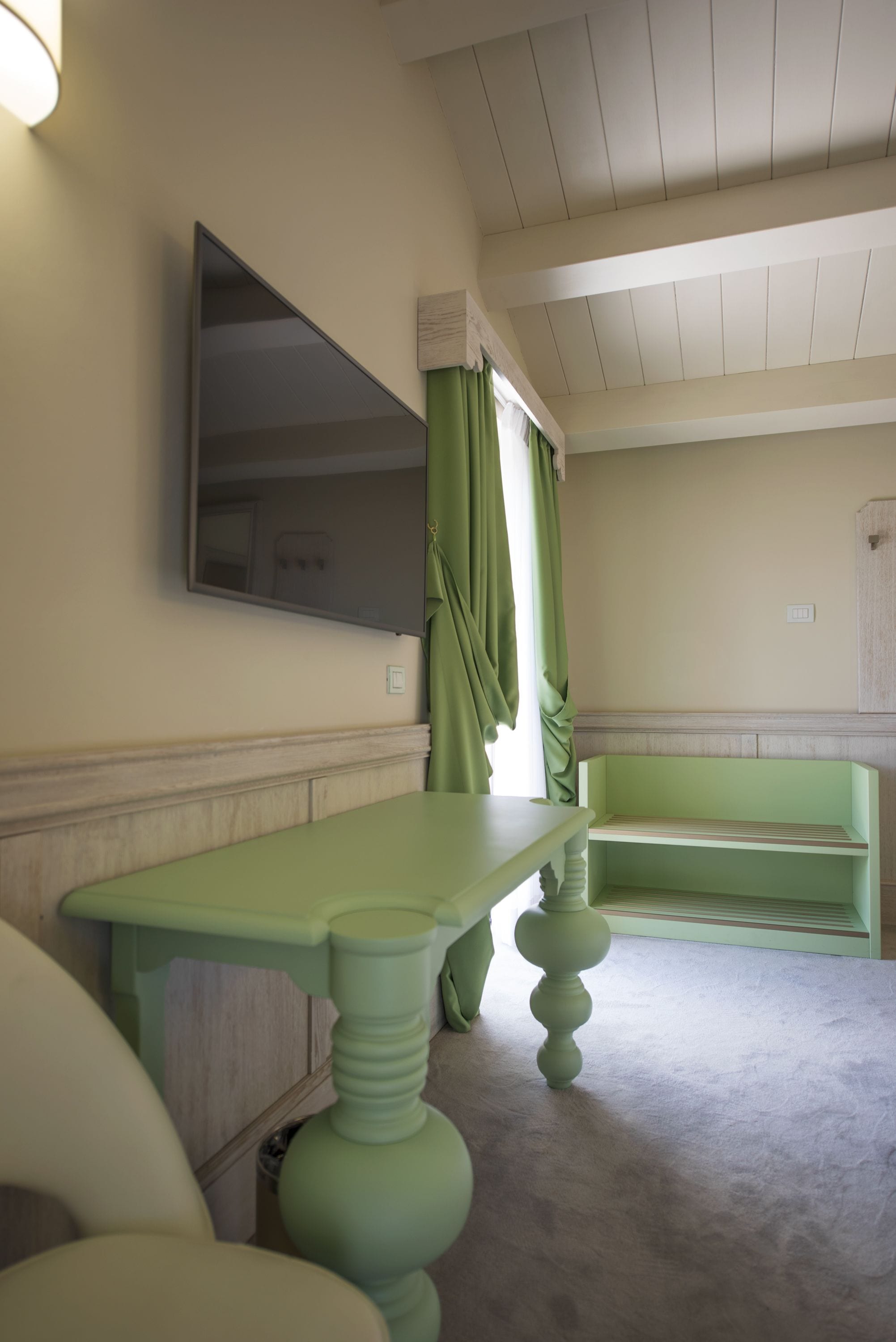A room with a green vanity, a mirror, a bench, and a light fixture on the wall.