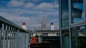 A balcony with a view of a tall, Gothic-style tower with multiple chimneys.