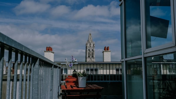 A balcony with a view of a tall, Gothic-style tower with multiple chimneys.