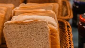 A basket of sliced bread on a table with jars of preserves in the background.