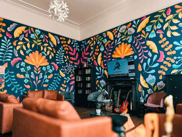 A room with a vibrant floral wall mural, leather furniture, a bookshelf, and a fireplace. - Gardiner House Hostel (Dublin)