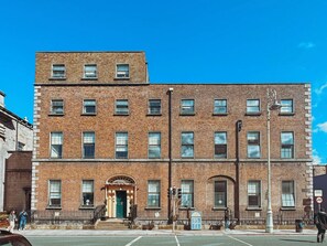 Un edificio de ladrillo de varios pisos con una entrada central, múltiples ventanas y vista a la calle.
