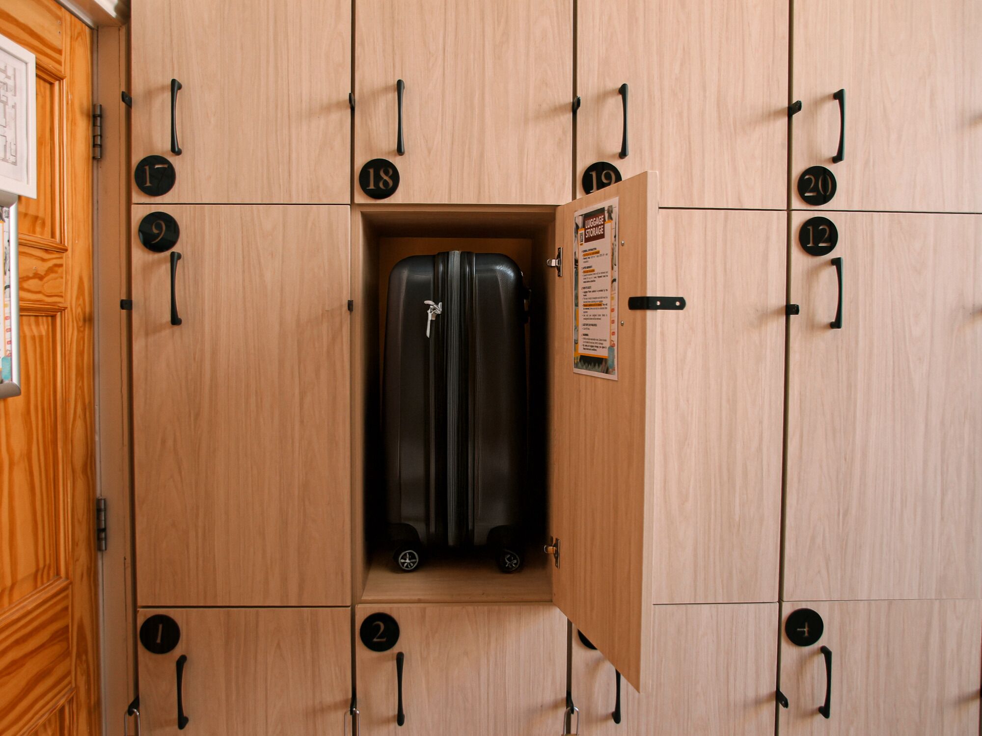 Un conjunto de taquillas de madera con compartimentos numerados, uno de los cuales contiene una maleta negra.
