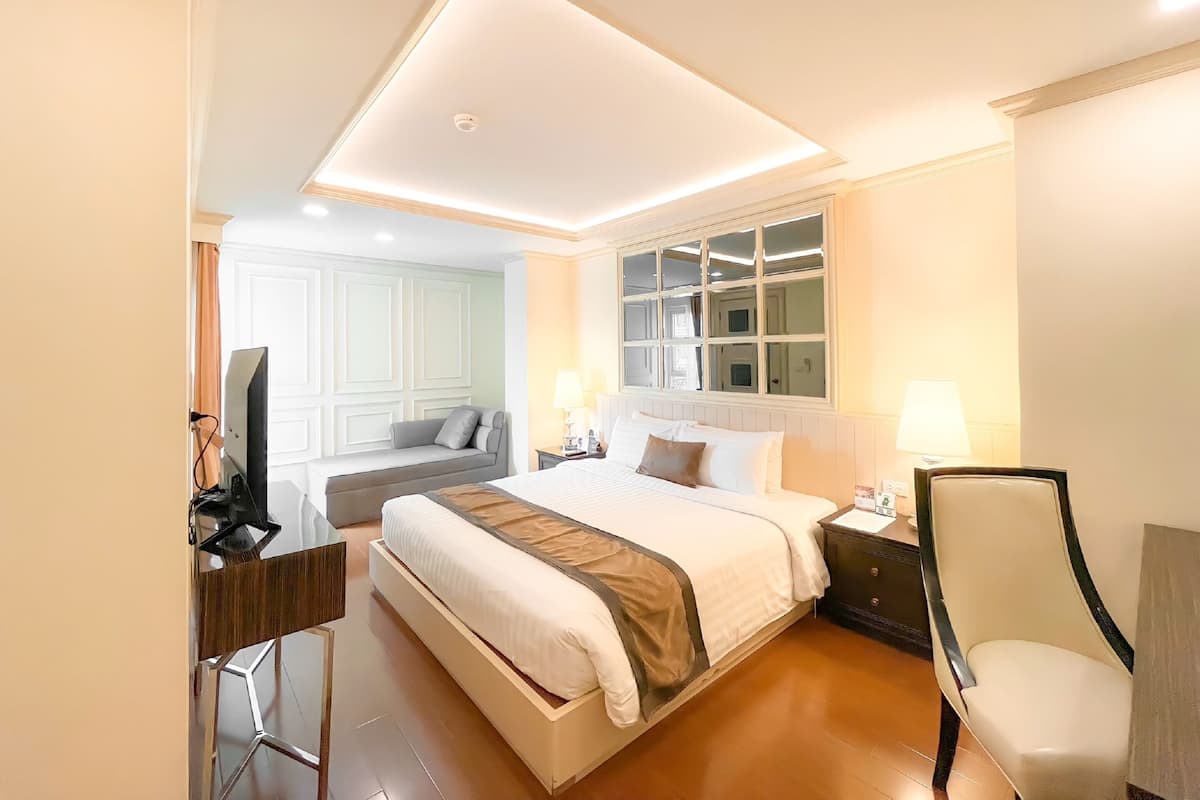 A hotel room with a large bed, a desk with a computer, a chair, a window with multiple panes, and a ceiling light.