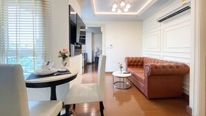 A modern living room with a brown leather sofa, a dining table with chairs, and a TV mounted on the wall.