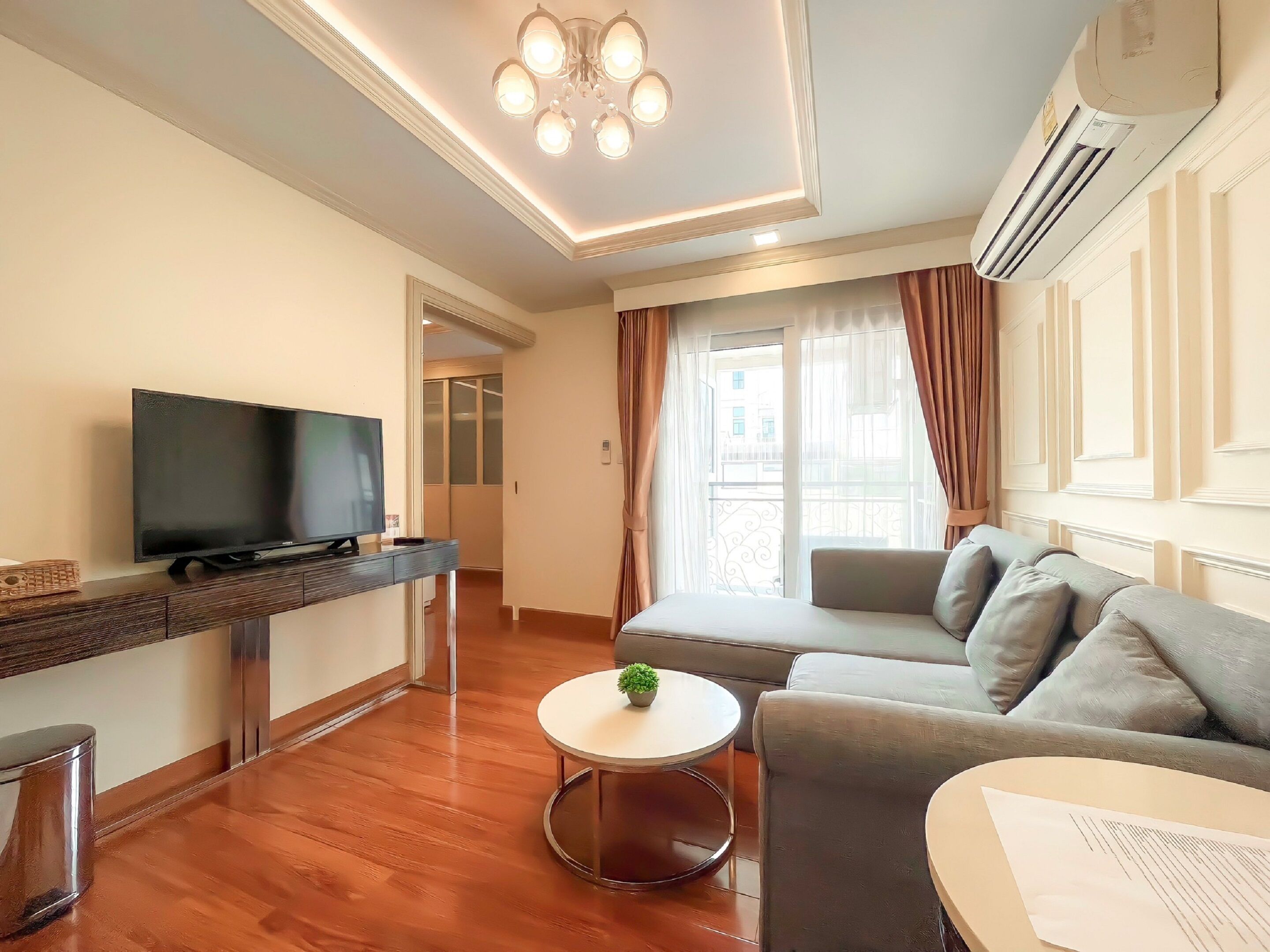 A modern living room with a flat-screen TV, a sofa, a coffee table, and a small plant.