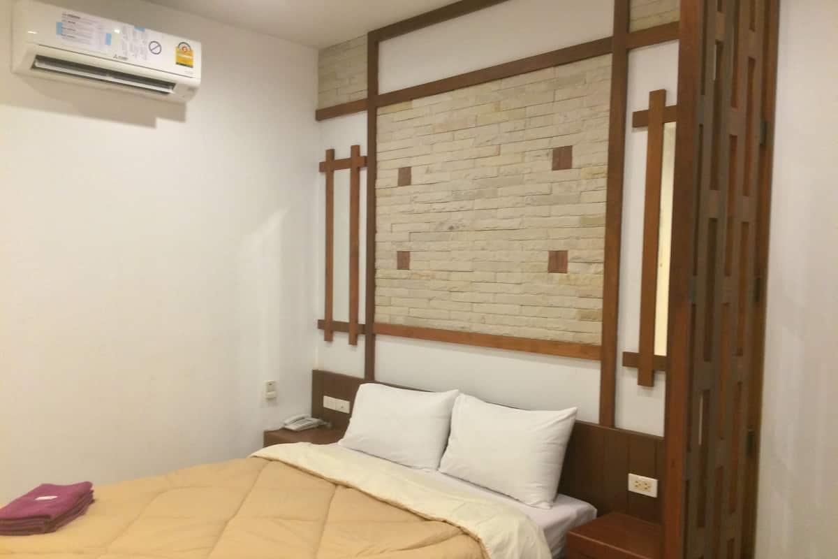 A hotel room with a bed, a wooden headboard, a brick-patterned wall, and an air conditioning unit.