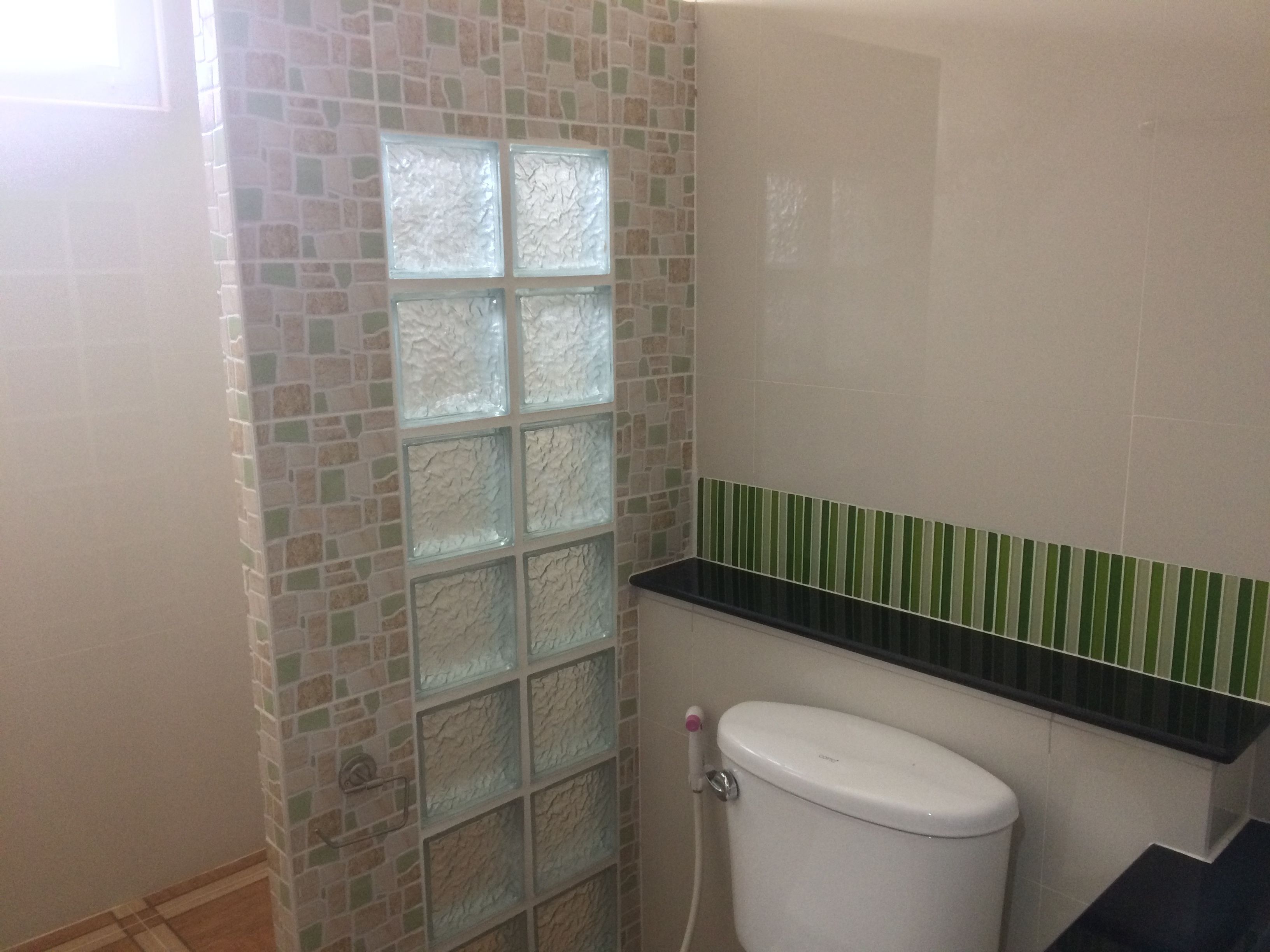 A bathroom with a tiled wall, a toilet, and a shower area.