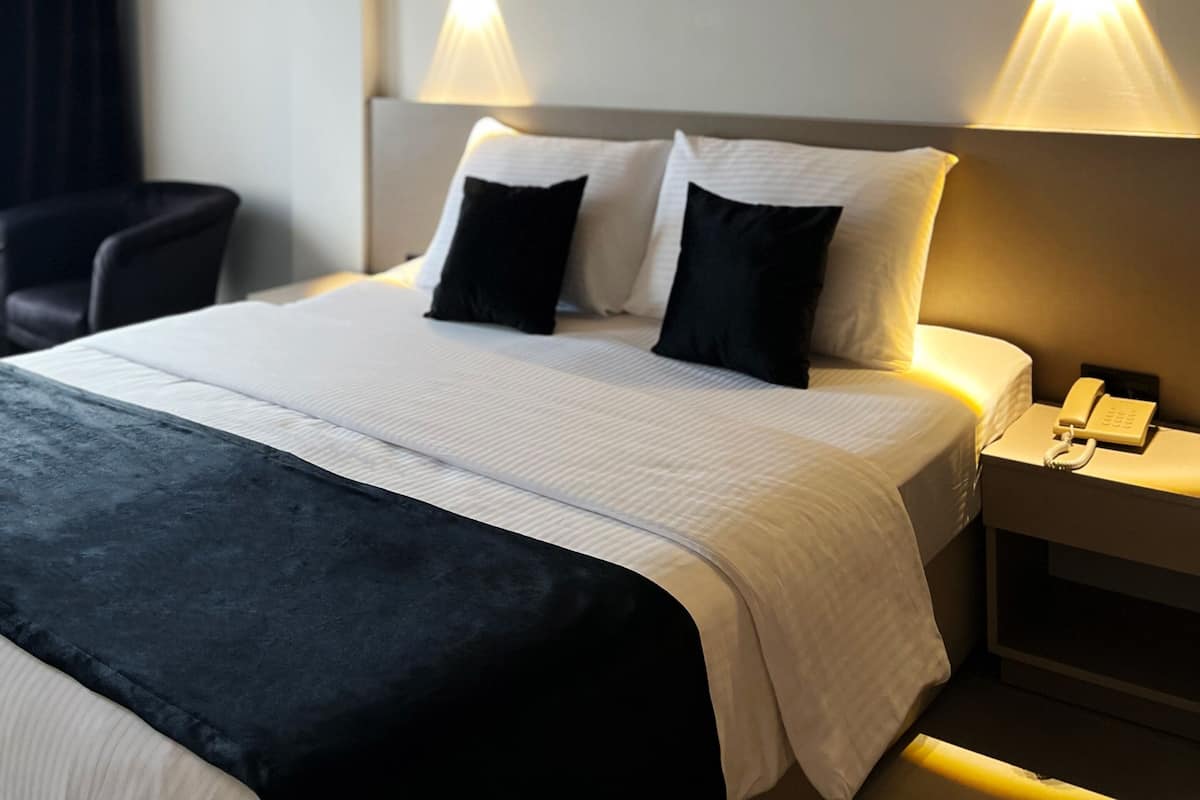 Une chambre d’hôtel avec un grand lit, deux lampes de chevet, une table de chevet avec un téléphone et une chaise.