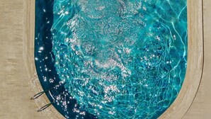 En person svømmer i en klar, blå pool med en flisebelagt terrasse hele vejen rundt.