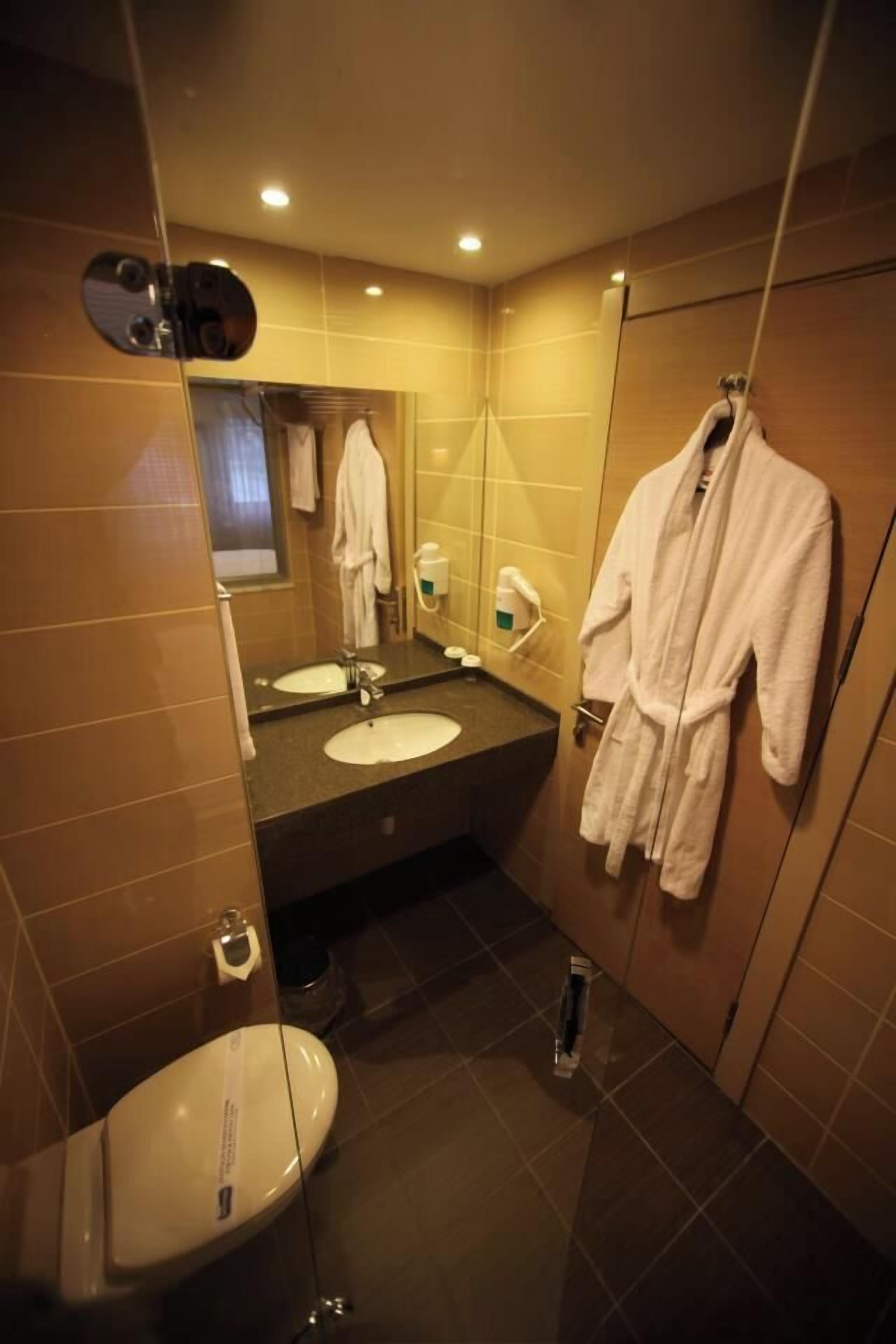 Un baño moderno con lavamanos doble, inodoro, espejo y bata colgada en la pared.