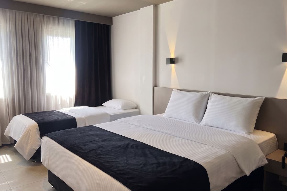 Une chambre d’hôtel avec deux lits, une grande fenêtre avec des rideaux et un luminaire fixé au mur.