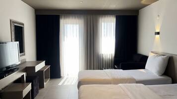 Een hotelkamer met twee bedden, een bureau, een televisie en een groot raam met gordijnen.