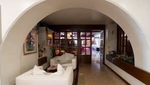 Um corredor com um sofá branco e uma mesa de centro, que leva a um quarto com uma janela grande e uma porta.