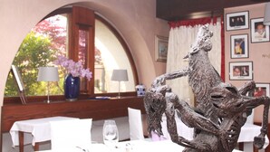 Uma mesa de jantar com um arranjo escultural no centro, um vaso com flores e quadros nas paredes.