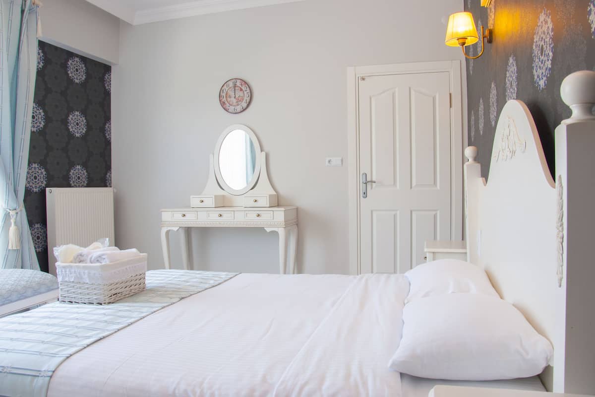 A bedroom with a bed, a dresser, a mirror, a wall clock, and a lamp.