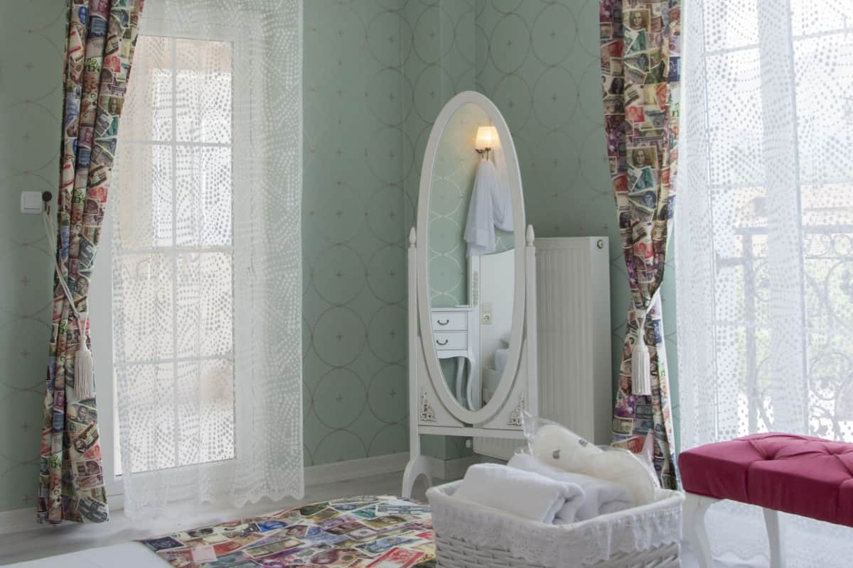 A bedroom with a bed, a white dresser, a mirror, a window with curtains, and a red bench.