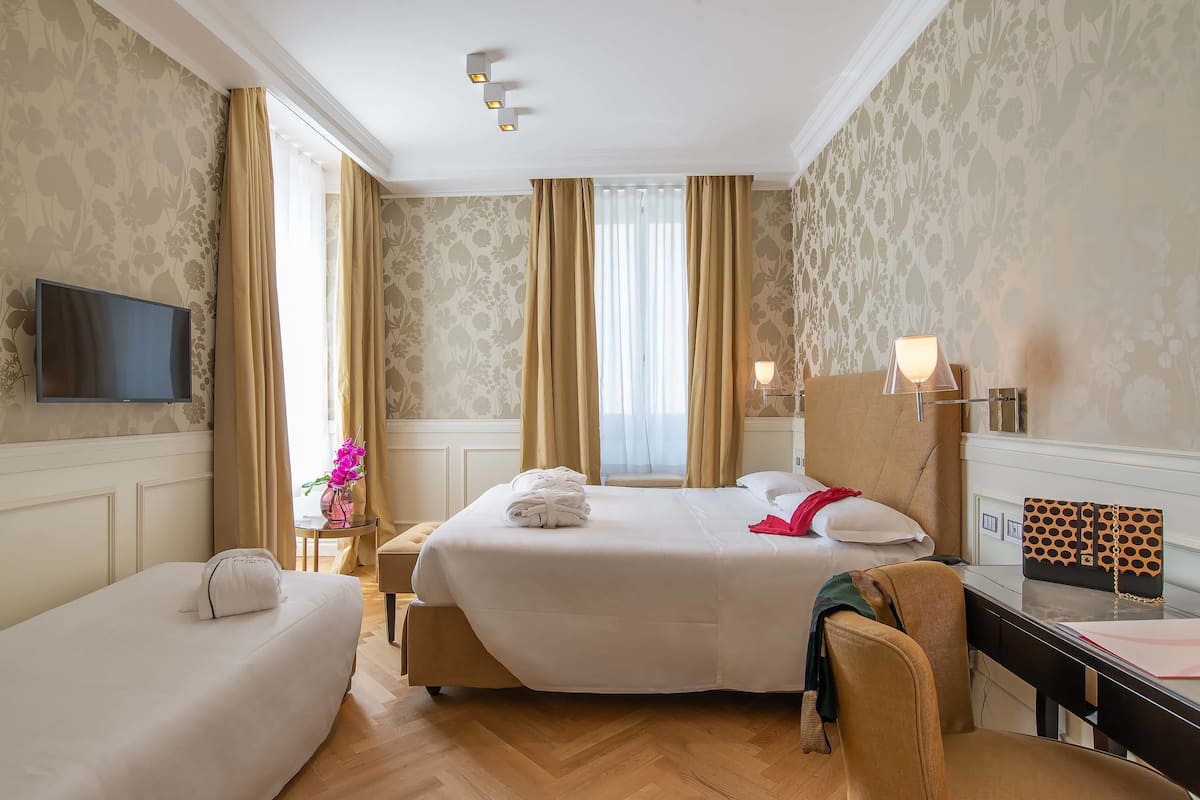 A hotel room with two beds, a desk, a TV, and a window with curtains.