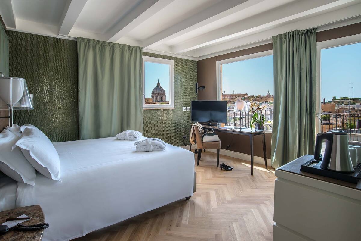 A hotel room with a bed, desk, and a view of a cityscape.