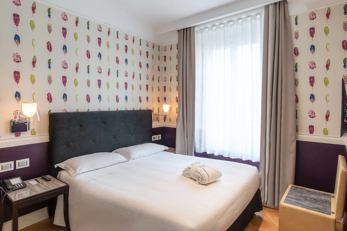 A neatly made bed with white linens, a folded towel, and a bedside table with a lamp and phone.