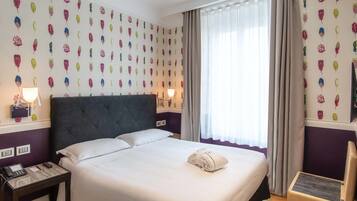 A neatly made bed with white linens, a folded towel, and a bedside table with a lamp and phone.
