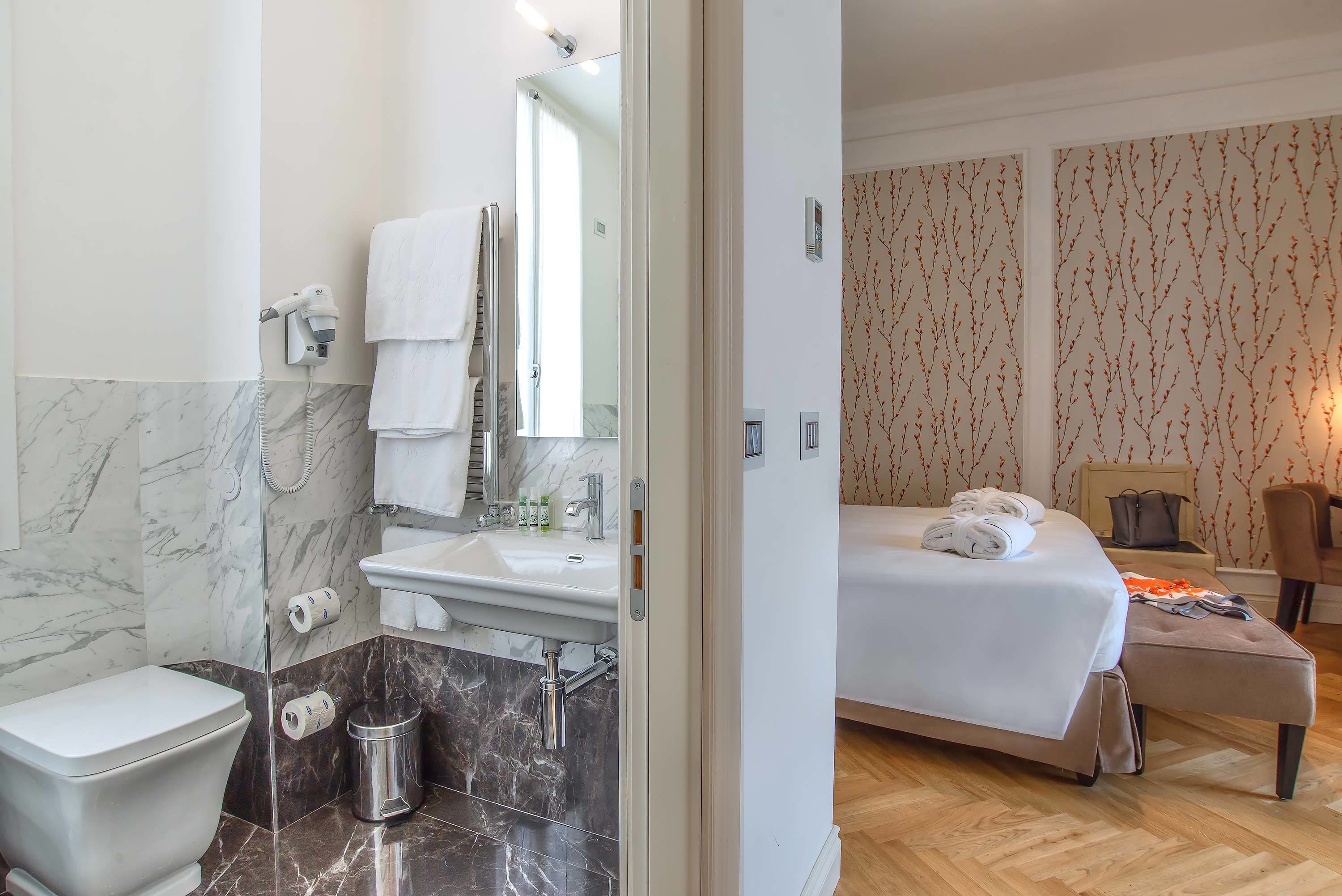 A hotel room with a bathroom, a bed, a bedside table, and a chair.