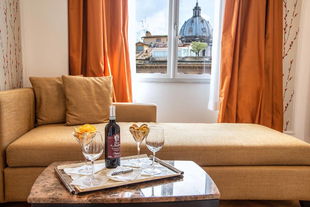 A room with a sofa, a tray with a bottle and glasses, and a window with a view of a building.