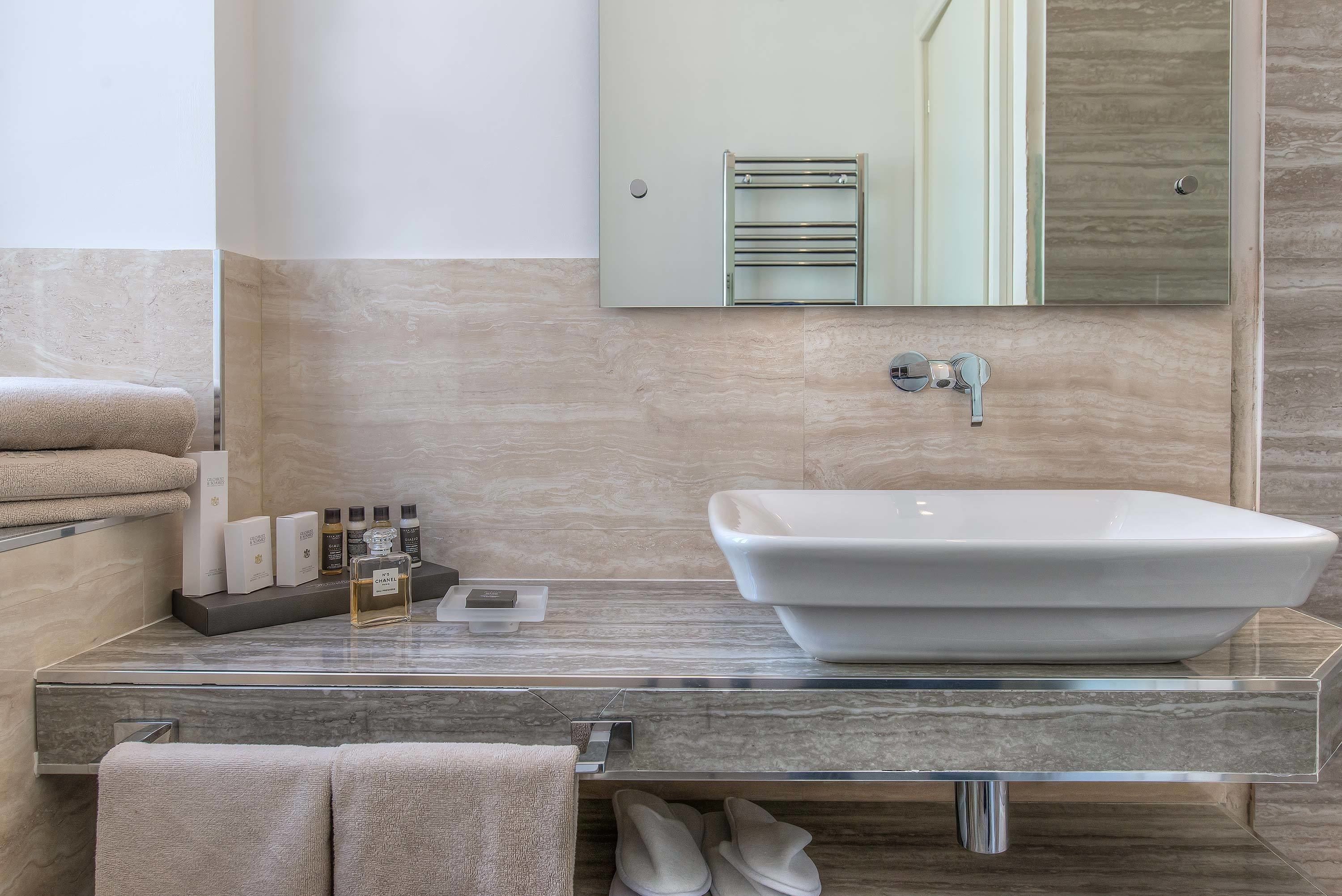 Un bagno moderno con un lavandino rettangolare grande, uno specchio sopra e un porta asciugamani a sinistra.