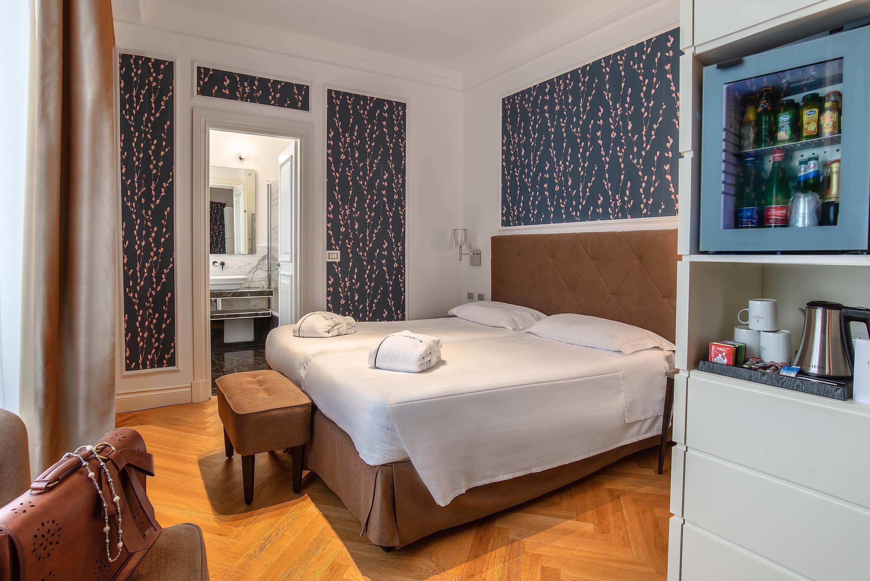Et hotelværelse med en seng, et lille bord, en bænk, et garderobeskab og en minibar.