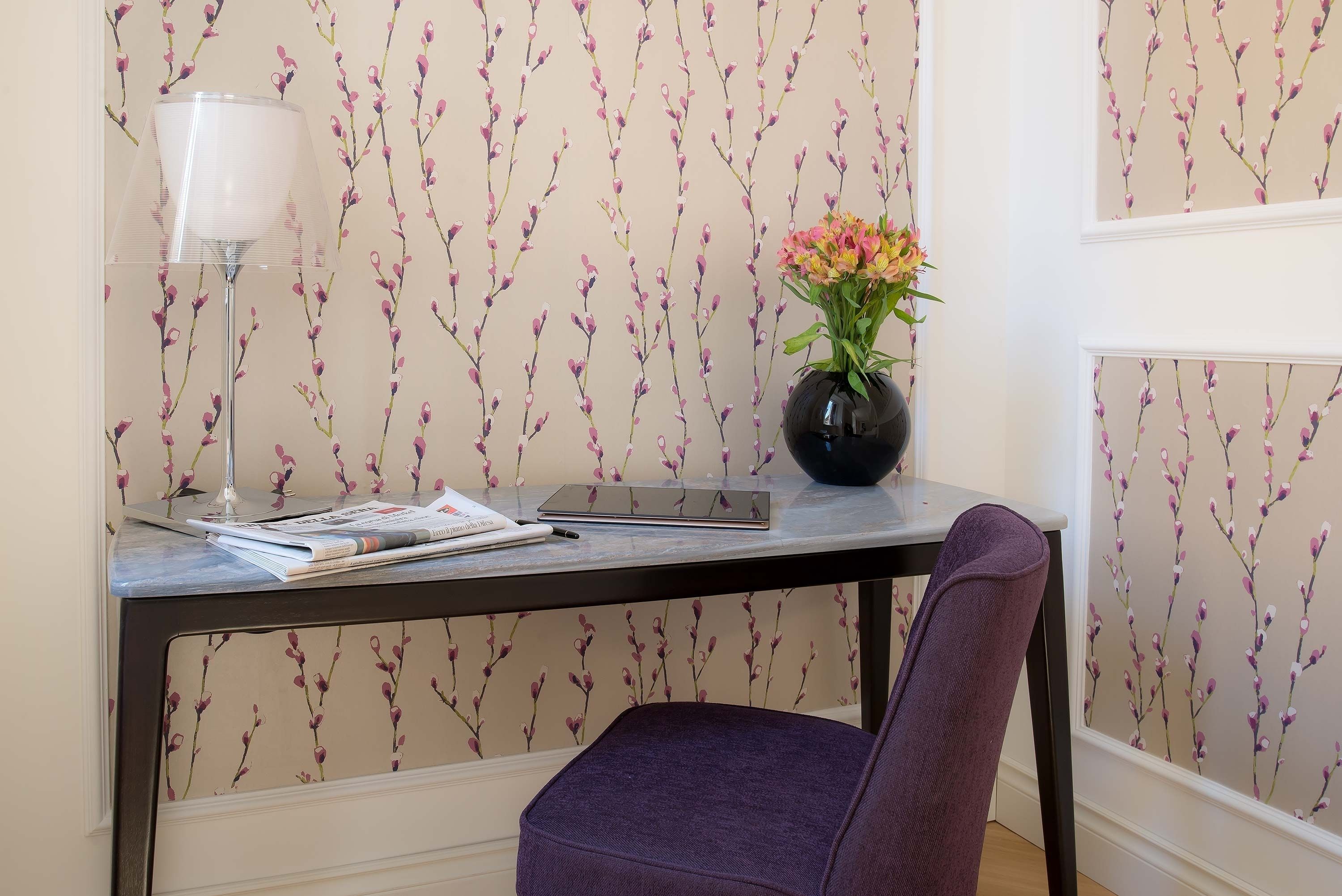 A desk with a lamp, a vase with flowers, and a chair.