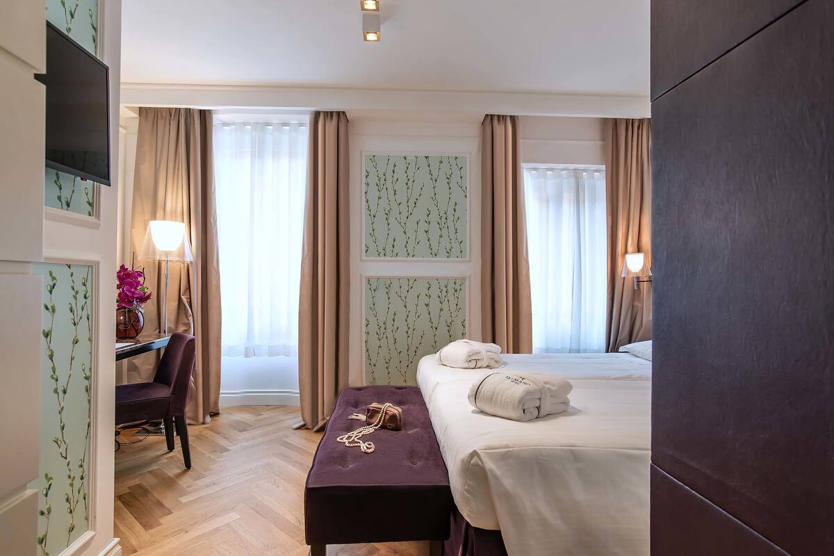 A hotel room with a bed, bedside table, lamp, and a desk with a chair.
